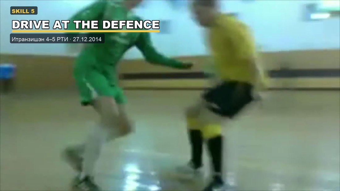 A player in a green kit driving at a defender in yellow on an indoor futsal court.