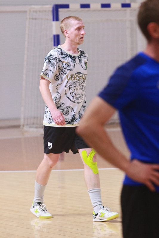 An EasyChamp player in white shaping to go past a defender in a blue shirt on a futsal court.