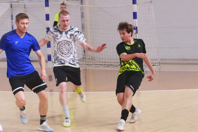 A scramble in front of the goal between players in white and in black and neon during a futsal match.