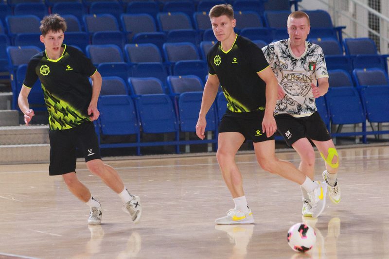 Three futsal players converging on the ball in midfield in a Minsk hall.