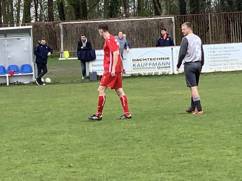 A player in the red SV Rangsdorf 28 kit on the ball with the touchline and spectators behind.