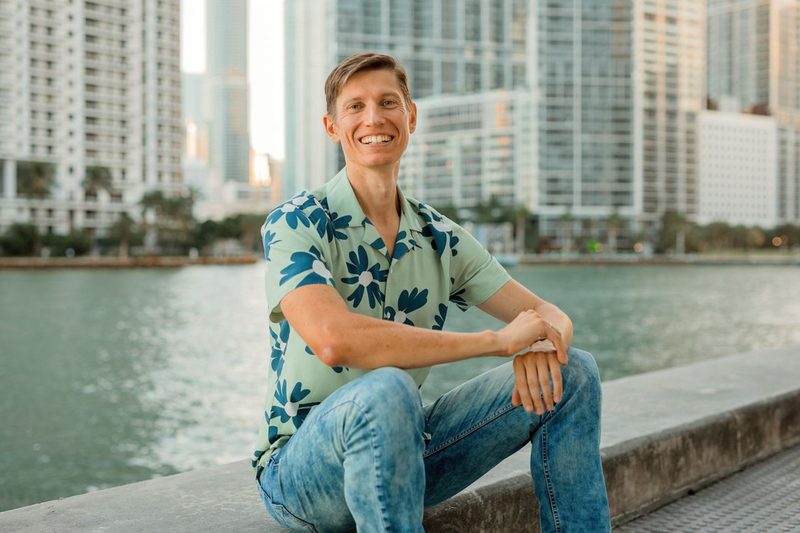 Anton Abyzov sitting on the Brickell waterfront in Miami with the skyline behind him.