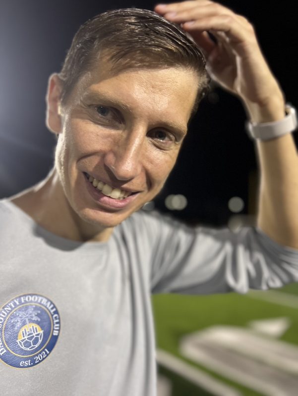 Portrait of Anton Abyzov in a Dade County FC top on the pitch at night.