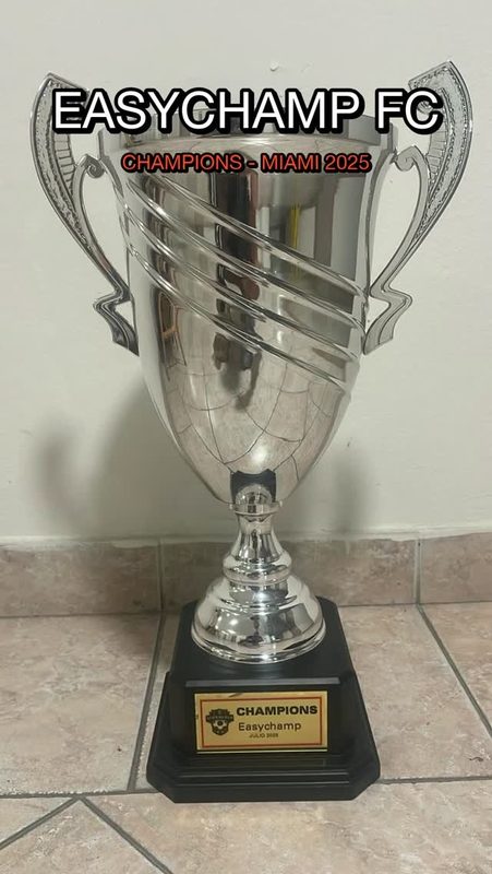 A silver cup on a wooden plinth with an EasyChamp FC champions plate.