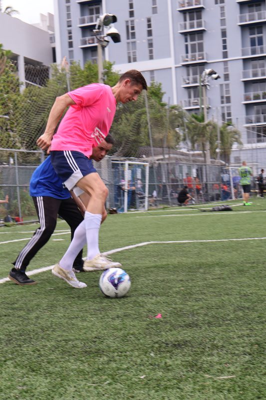 Anton Abyzov in a pink kit driving past a defender on a Miami pitch with towers behind.