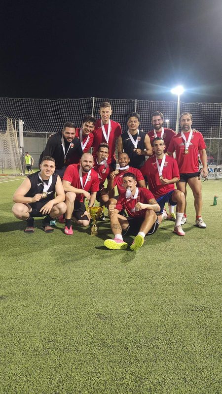 The Team Patagonia squad in red kit with medals around their necks on a floodlit pitch.