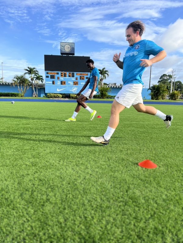 Anton Abyzov running with the ball in a light blue kit on the turf at Traz Powell Stadium.