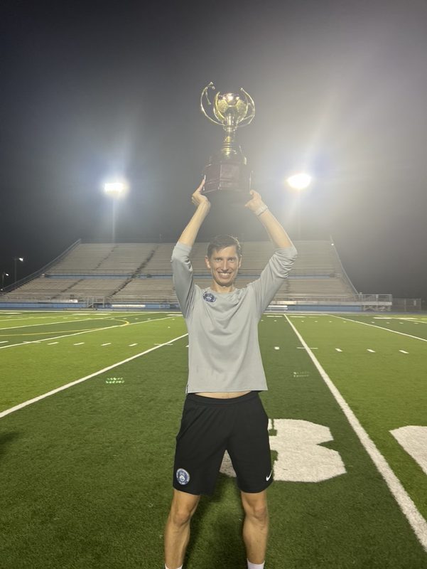 Anton Abyzov lifting the USSL trophy over his head on the pitch at night.