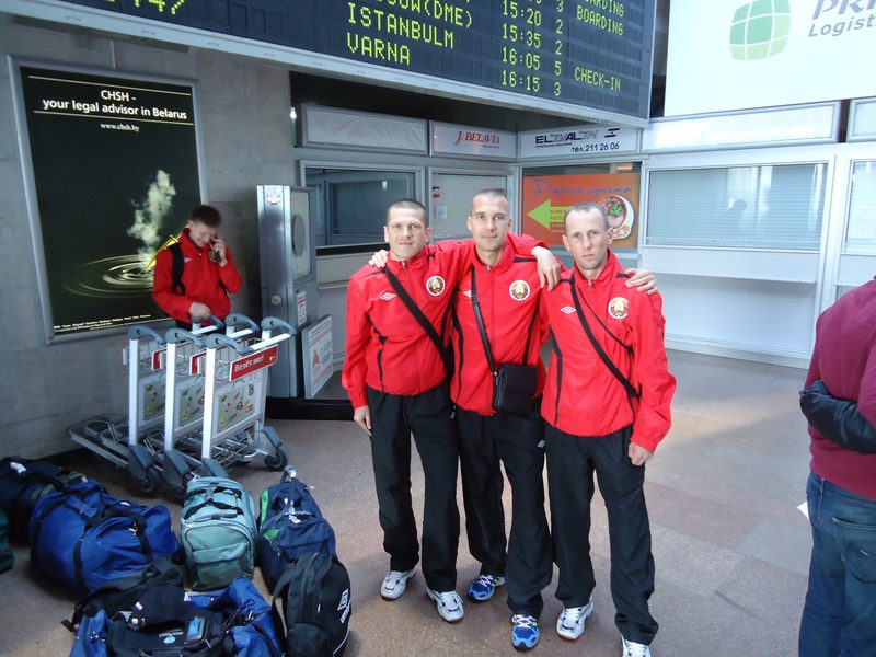 Players in red Belarus tracksuits standing over team kitbags in an airport departure hall.