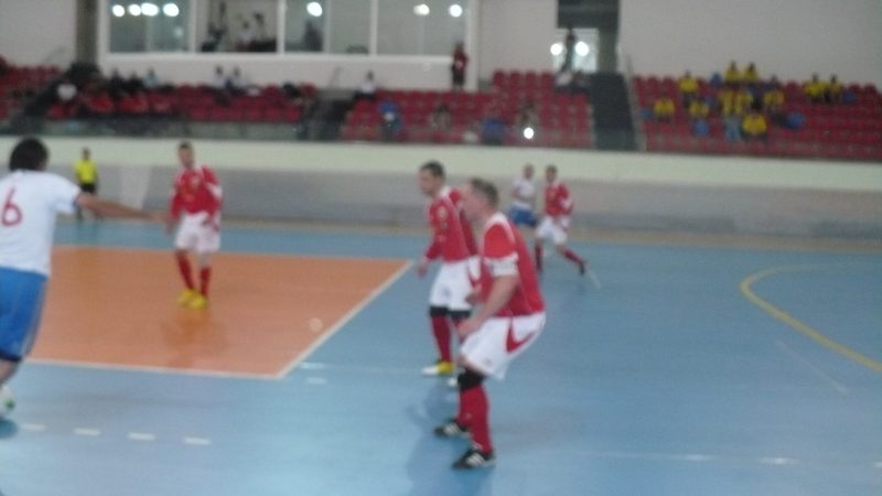 A wide view of a futsal match in progress in the Kayseri hall, players in red and white on a blue court.