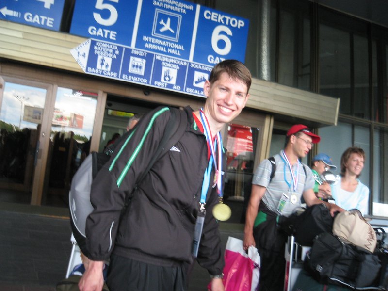 Anton Abyzov smiling in the international arrivals hall at Minsk airport with the 2009 European Championship gold medal round his neck and a kitbag over his shoulder.