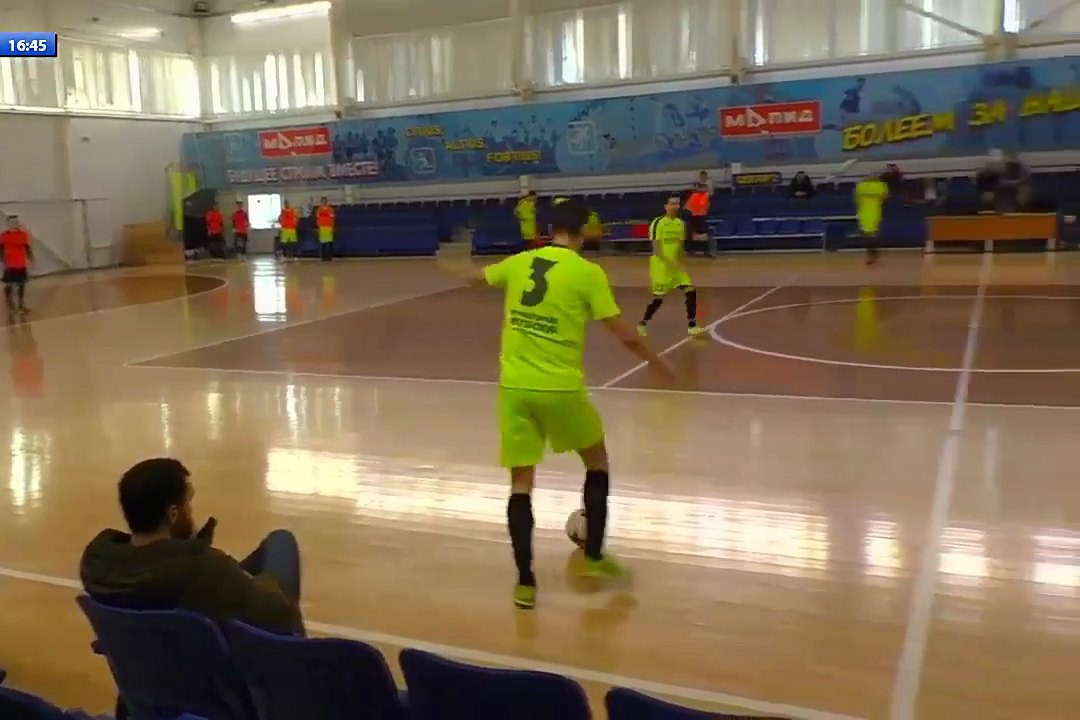 Futsal match at SK MAPID in Minsk, a player in a light green kit on the ball with the court and the stand behind.